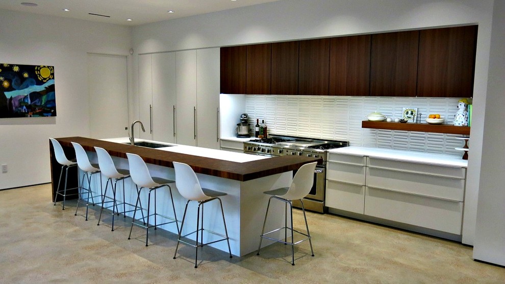 Photo of a mid-sized midcentury galley eat-in kitchen in Houston with an undermount sink, flat-panel cabinets, white cabinets, quartz benchtops, white splashback, ceramic splashback, stainless steel appliances, concrete floors and with island.