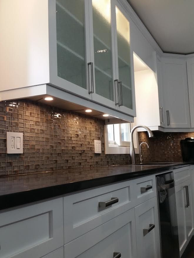 Example of a mid-sized transitional kitchen design with an undermount sink, shaker cabinets, white cabinets, brown backsplash, glass tile backsplash, stainless steel appliances and an island