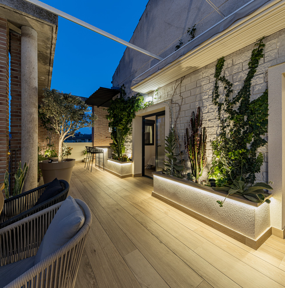 Inspiration for a large contemporary courtyard and rooftop deck in Seville with an awning and metal railing.