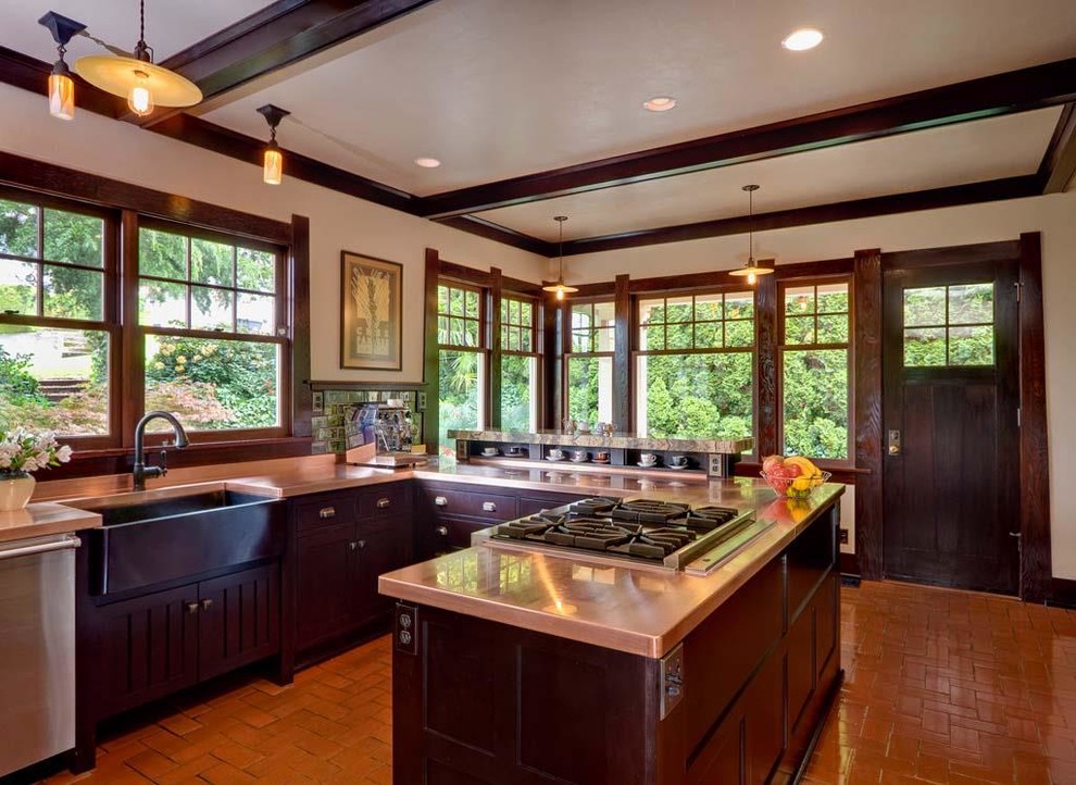 Photo of an arts and crafts u-shaped kitchen in Seattle with a farmhouse sink, shaker cabinets, dark wood cabinets, copper benchtops, green splashback, ceramic splashback, stainless steel appliances, terra-cotta floors and a peninsula.