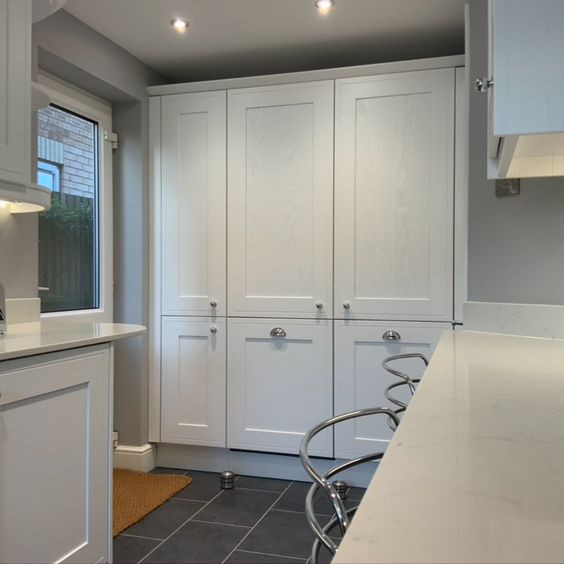 Modelo de cocina tradicional, pequeña, con armarios estilo shaker, puertas de armario blancas, encimera de cuarcita, salpicadero blanco, puertas de cuarzo sintético, electrodomésticos con paneles, suelo vinílico, península, suelo gris y encimeras blancas