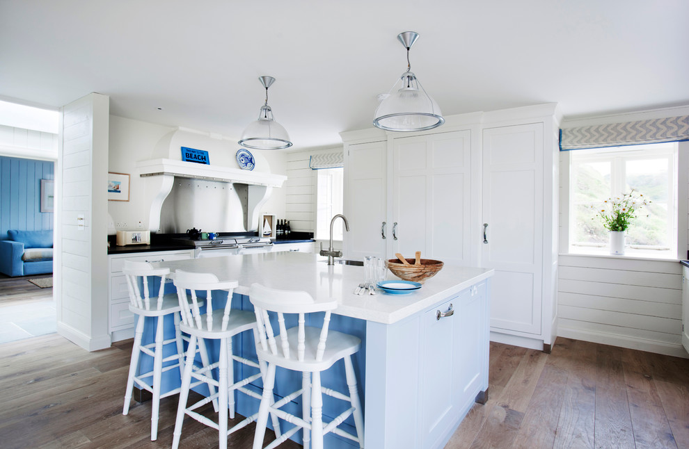 Inspiration for a beach style u-shaped kitchen in Wiltshire with a farmhouse sink, recessed-panel cabinets, white cabinets, panelled appliances, medium hardwood floors, with island and brown floor.
