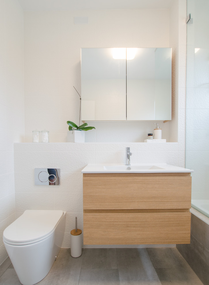 Photo of a small contemporary bathroom in Sydney with flat-panel cabinets, light wood cabinets, a drop-in tub, a shower/bathtub combo, gray tile, ceramic tile, engineered quartz benchtops, a two-piece toilet, white walls, cement tiles and a drop-in sink.