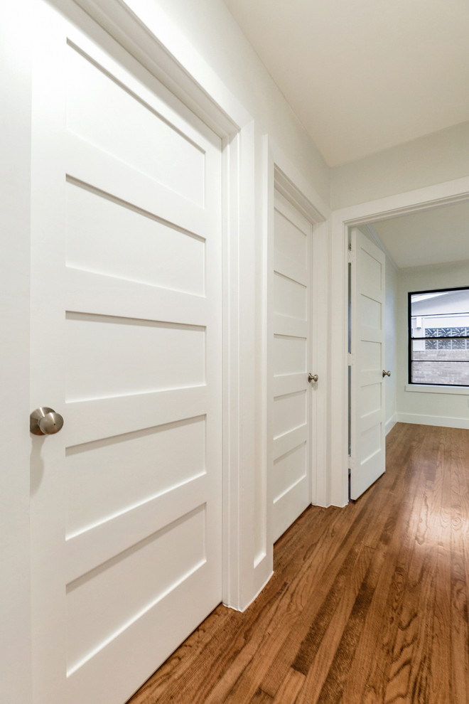 Design ideas for a mid-sized transitional hallway in Dallas with white walls, light hardwood floors and brown floor.