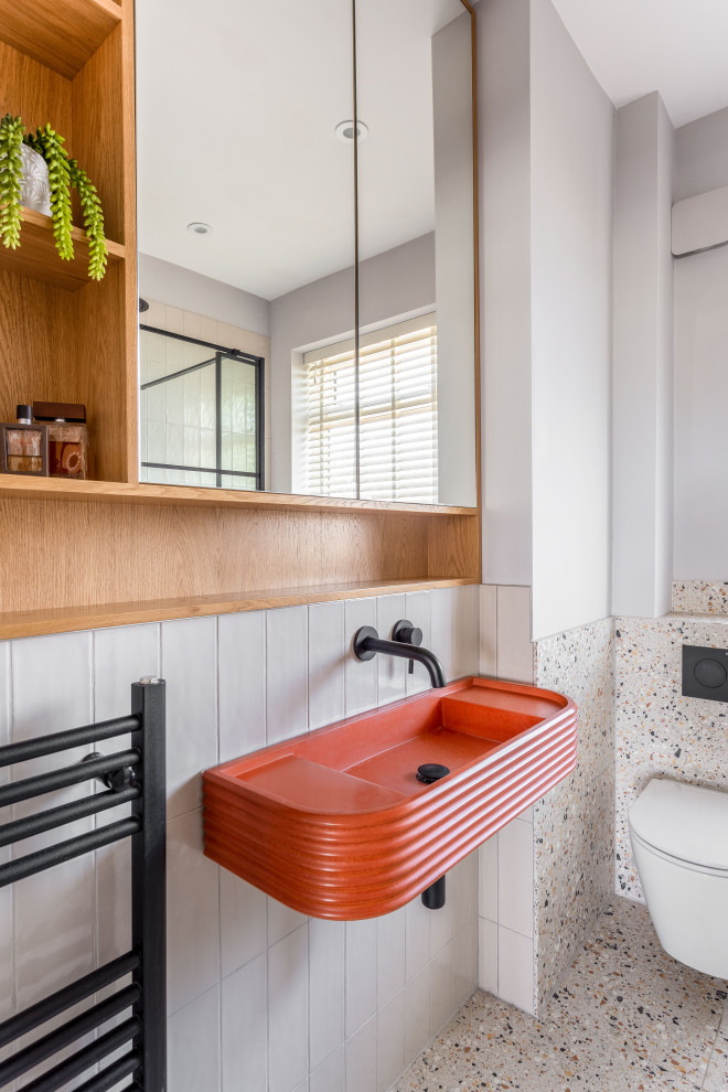 Eklektisk inredning av ett litet orange oranget badrum med dusch, med orange skåp, en öppen dusch, en vägghängd toalettstol, grå kakel, keramikplattor, grå väggar, terrazzogolv, ett väggmonterat handfat, bänkskiva i betong, orange golv och dusch med gångjärnsdörr