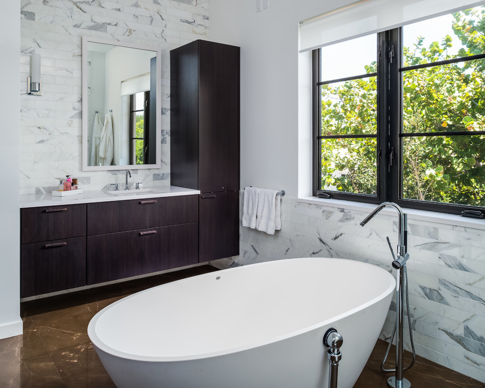 Design ideas for a contemporary bathroom in Miami with an undermount sink, flat-panel cabinets, dark wood cabinets, a freestanding tub, gray tile and white walls.