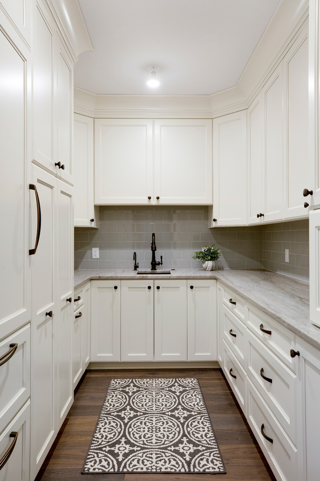 Photo of an expansive traditional u-shaped kitchen pantry in Minneapolis with an undermount sink, raised-panel cabinets, white cabinets, solid surface benchtops, white splashback, ceramic splashback, panelled appliances, medium hardwood floors, multiple islands and white benchtop.