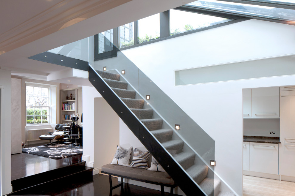 This is an example of a mid-sized contemporary carpeted straight staircase in London with carpet risers and glass railing.