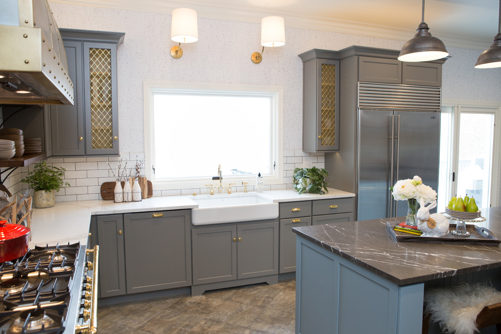 This is an example of a large transitional u-shaped eat-in kitchen in Chicago with a farmhouse sink, shaker cabinets, grey cabinets, limestone benchtops, white splashback, subway tile splashback, black appliances, porcelain floors, with island and grey floor.
