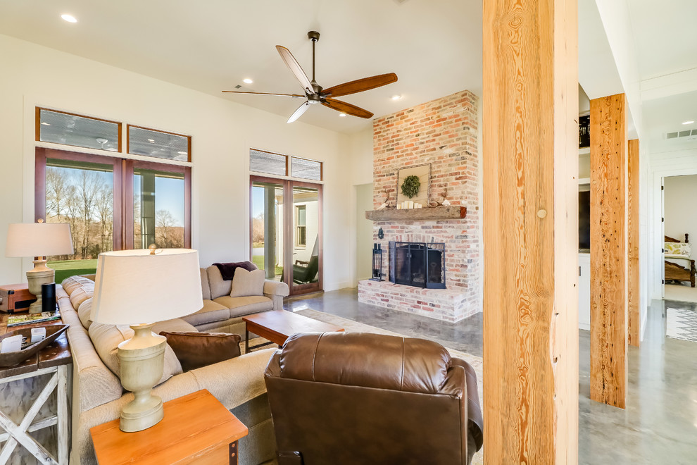 This is an example of a large country open concept living room in Jackson with white walls, concrete floors, a standard fireplace, a brick fireplace surround, a built-in media wall and grey floor.