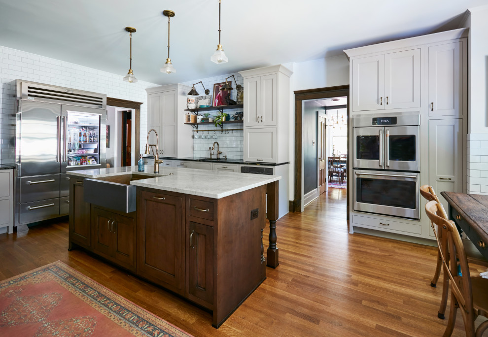 Photo of a mid-sized traditional u-shaped eat-in kitchen in New York with a farmhouse sink, beaded inset cabinets, quartzite benchtops, white splashback, ceramic splashback, stainless steel appliances, medium hardwood floors, with island, brown floor and green benchtop.