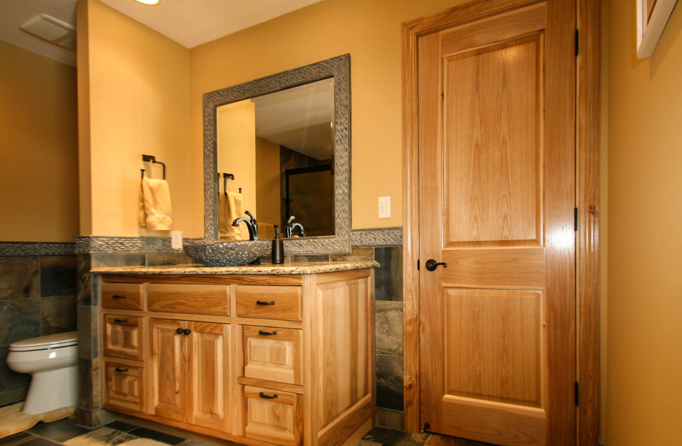 This is an example of a mid-sized country kids bathroom in Minneapolis with a vessel sink, raised-panel cabinets, light wood cabinets, granite benchtops, a drop-in tub, a shower/bathtub combo, a two-piece toilet, multi-coloured tile, stone tile, yellow walls and slate floors.