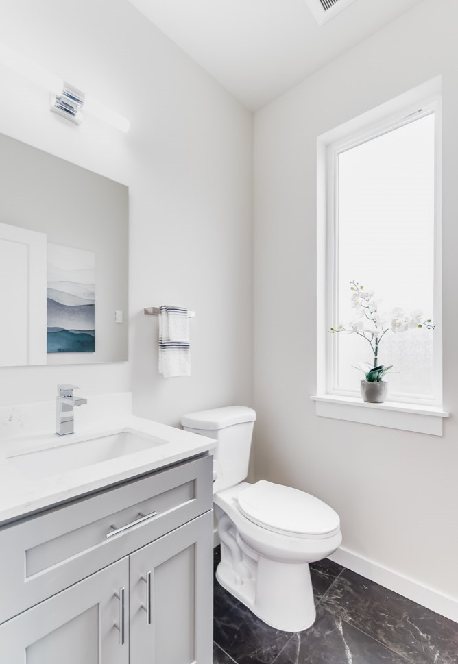 Inspiration for a mid-sized contemporary powder room in New York with furniture-like cabinets, grey cabinets, a one-piece toilet, white walls, marble floors, a drop-in sink, engineered quartz benchtops, grey floor, white benchtops and a freestanding vanity.
