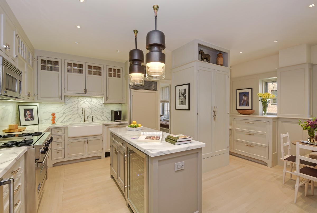 This is an example of a transitional u-shaped eat-in kitchen in New York with a farmhouse sink, shaker cabinets, grey cabinets, white splashback, marble splashback, panelled appliances, light hardwood floors, with island, beige floor and marble benchtops.