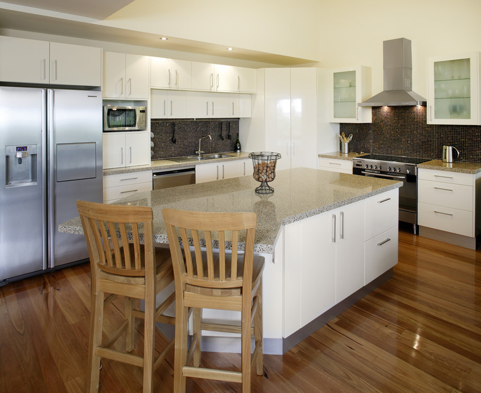 Enclosed kitchen - large transitional l-shaped medium tone wood floor and brown floor enclosed kitchen idea in DC Metro with a drop-in sink, flat-panel cabinets, white cabinets, terrazzo countertops, black backsplash, mosaic tile backsplash, stainless steel appliances and an island