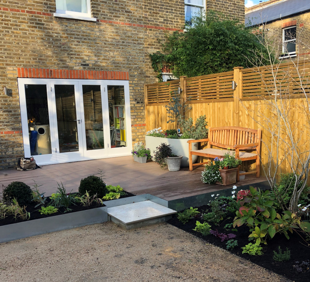 Photo of a contemporary backyard garden in London with natural stone pavers and a wood fence.