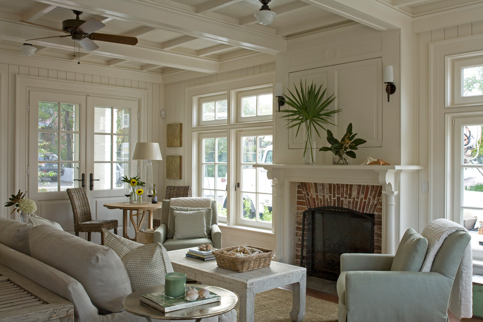 Photo of a beach style living room in Other with white walls, medium hardwood floors, a standard fireplace, a brick fireplace surround, a concealed tv and white floor.