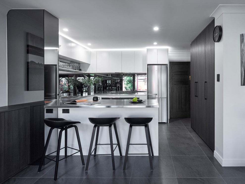 This is an example of a large modern u-shaped eat-in kitchen in Other with an integrated sink, white cabinets, stainless steel benchtops, glass sheet splashback, stainless steel appliances, ceramic floors and a peninsula.