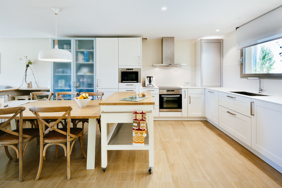 Photo of a transitional kitchen in Barcelona with white cabinets, white splashback, stainless steel appliances, with island and white benchtop.