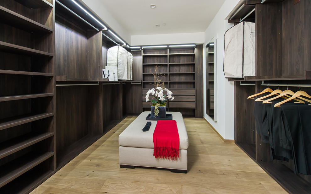 Large modern gender-neutral walk-in wardrobe in Los Angeles with open cabinets, dark wood cabinets and light hardwood floors.