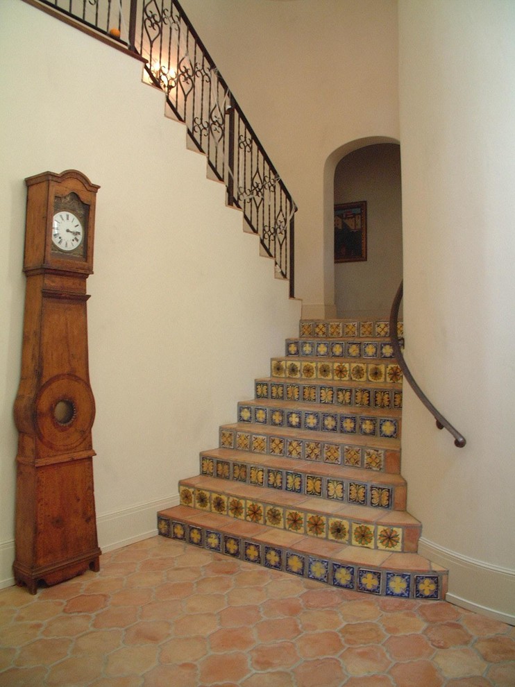 Mid-sized mediterranean terracotta u-shaped staircase in Houston with tile risers and metal railing.