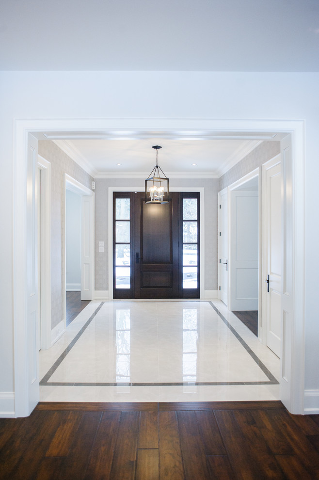 This is an example of a mid-sized contemporary foyer in Toronto with white walls, marble floors, a single front door, a dark wood front door and brown floor.