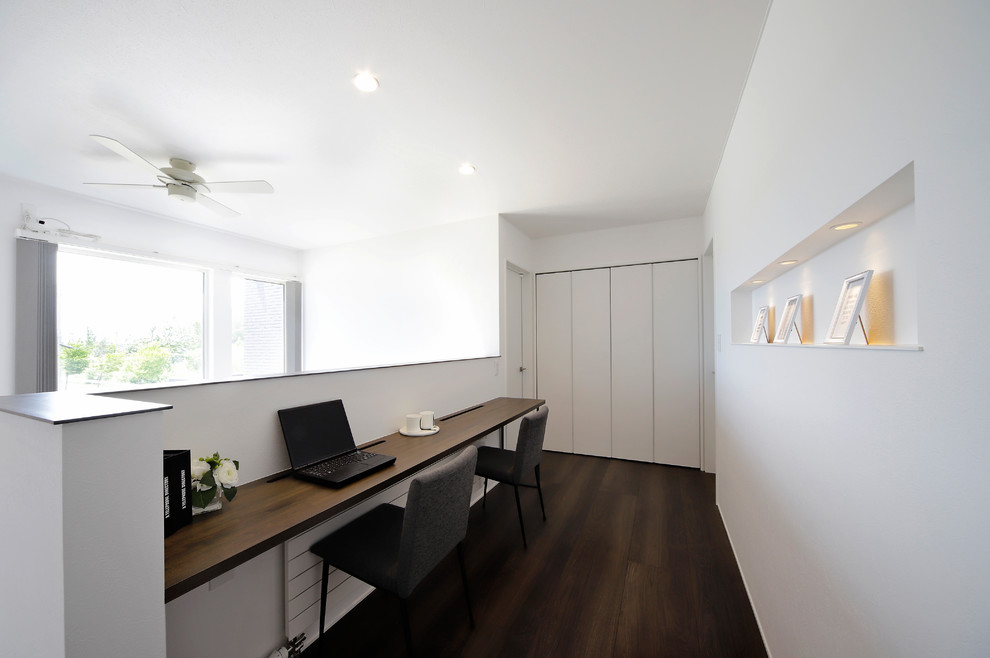 Asian home office in Sapporo with white walls, dark hardwood floors, a built-in desk and brown floor.