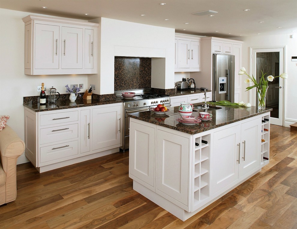 This is an example of a large traditional single-wall eat-in kitchen in Hampshire with a drop-in sink, shaker cabinets, white cabinets, granite benchtops, brown splashback, stone slab splashback, stainless steel appliances, with island, brown benchtop, medium hardwood floors and brown floor.