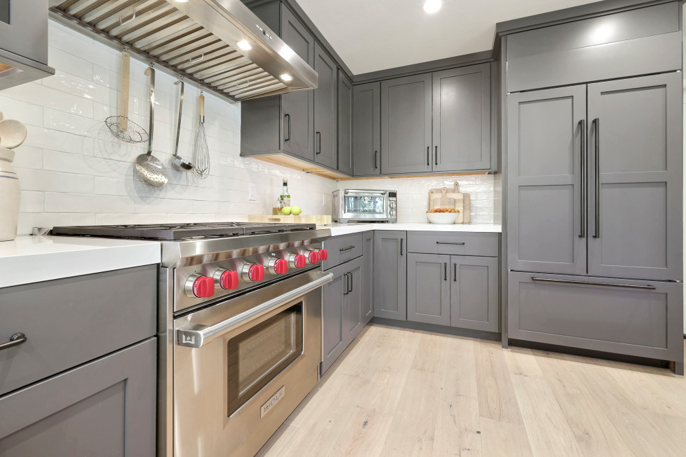 Inspiration for a mid-sized transitional l-shaped laminate floor open concept kitchen remodel with a double-bowl sink, flat-panel cabinets, gray cabinets, quartz countertops, white backsplash, ceramic backsplash, stainless steel appliances, an island and white countertops