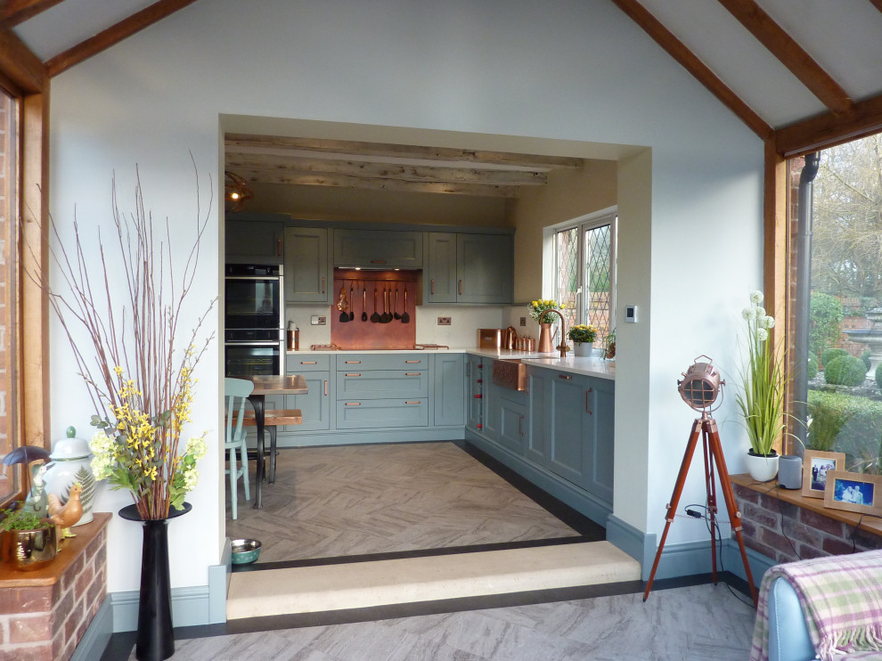 Inspiration for a large transitional galley eat-in kitchen in West Midlands with a farmhouse sink, beaded inset cabinets, blue cabinets, quartzite benchtops, orange splashback, black appliances, vinyl floors, with island, grey floor, white benchtop and exposed beam.