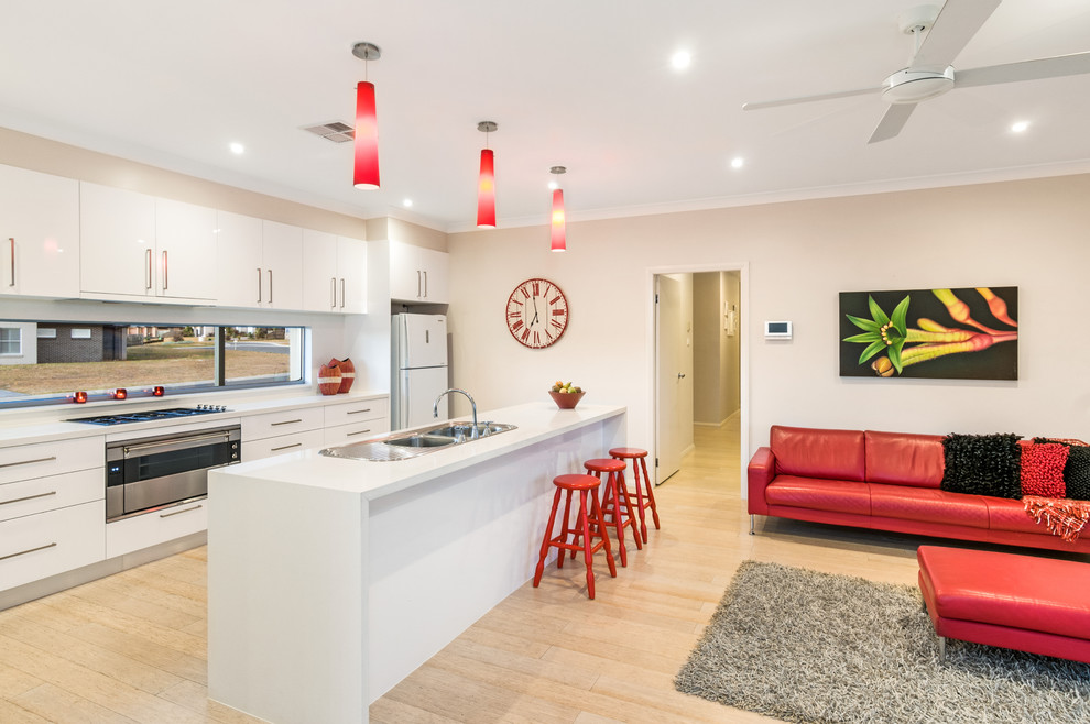 Mid-sized modern galley open plan kitchen in Sydney with a double-bowl sink, white cabinets, quartz benchtops, stainless steel appliances, light hardwood floors and with island.