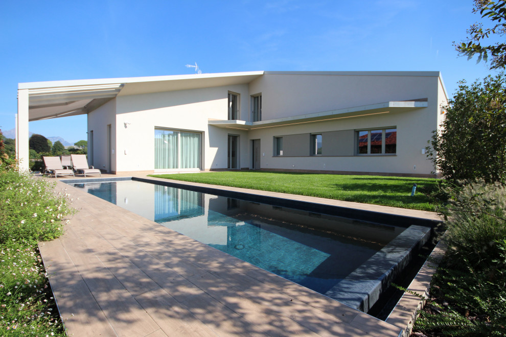 Ejemplo de piscina infinita actual grande rectangular en patio delantero con paisajismo de piscina y adoquines de ladrillo