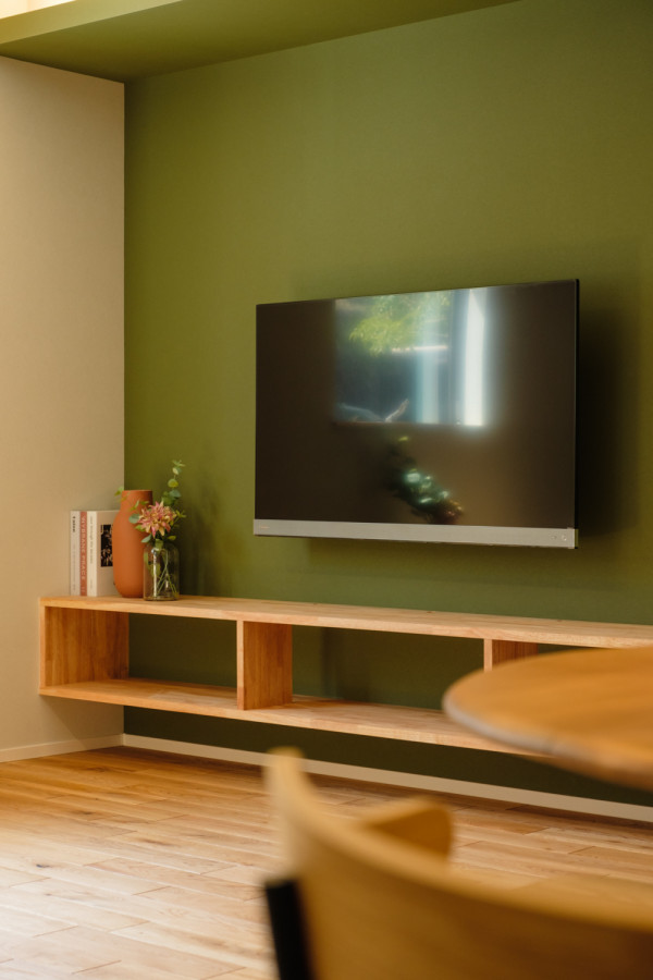 Inredning av ett vardagsrum, med gröna väggar, mellanmörkt trägolv, en väggmonterad TV och beiget golv