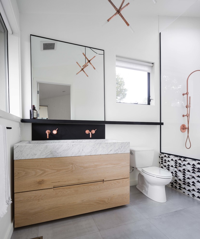 Inspiration for a mid-sized contemporary master bathroom in Los Angeles with flat-panel cabinets, light wood cabinets, a freestanding tub, white tile, porcelain tile, marble benchtops, grey benchtops, an alcove shower, a two-piece toilet, white walls, a trough sink and grey floor.
