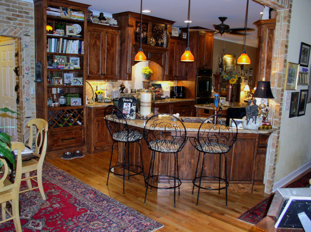 Mid-sized galley medium tone wood floor and brown floor kitchen photo in Atlanta with an undermount sink, raised-panel cabinets, medium tone wood cabinets, granite countertops, stainless steel appliances, an island and multicolored countertops