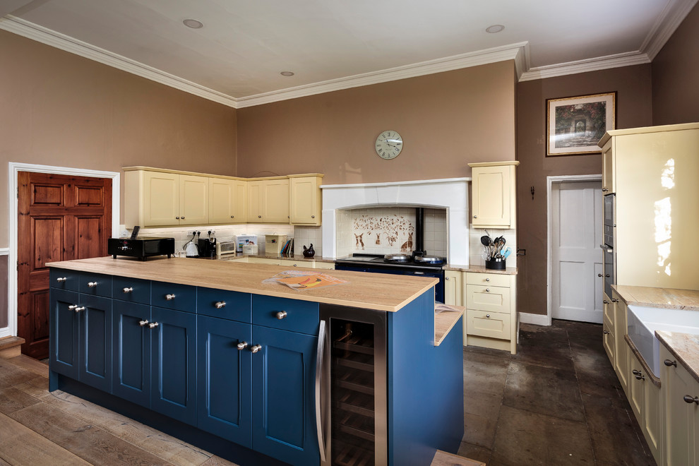 Inspiration for a large traditional kitchen in Other with a farmhouse sink, wood benchtops, with island, shaker cabinets, yellow cabinets, multi-coloured splashback, black appliances and brown floor.