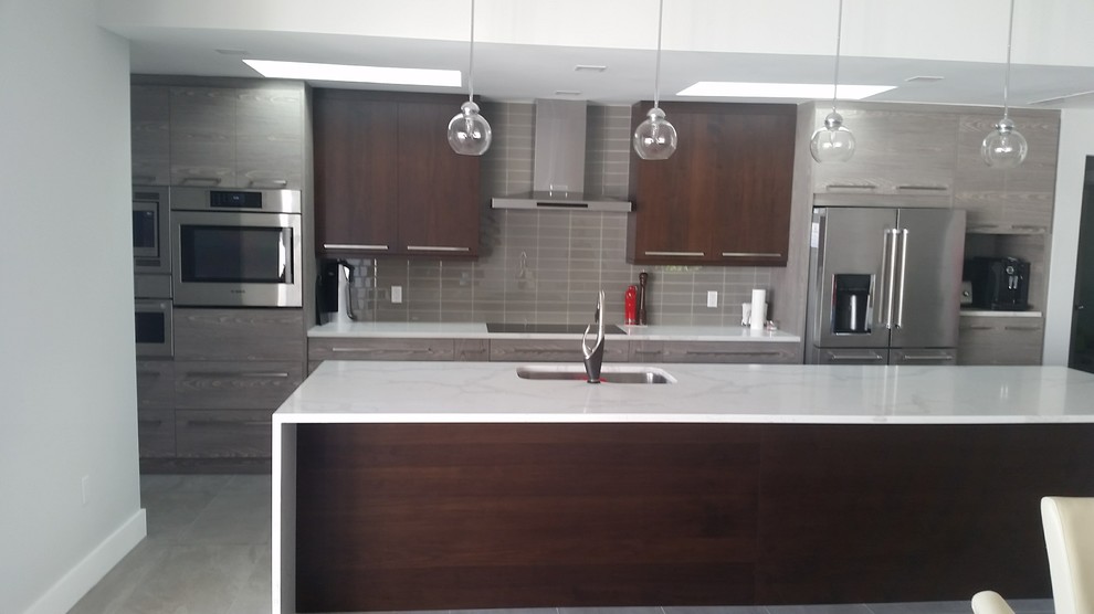 Mid-sized modern galley open plan kitchen in Tampa with a single-bowl sink, flat-panel cabinets, medium wood cabinets, quartz benchtops, beige splashback, glass tile splashback, stainless steel appliances, porcelain floors, with island and grey floor.