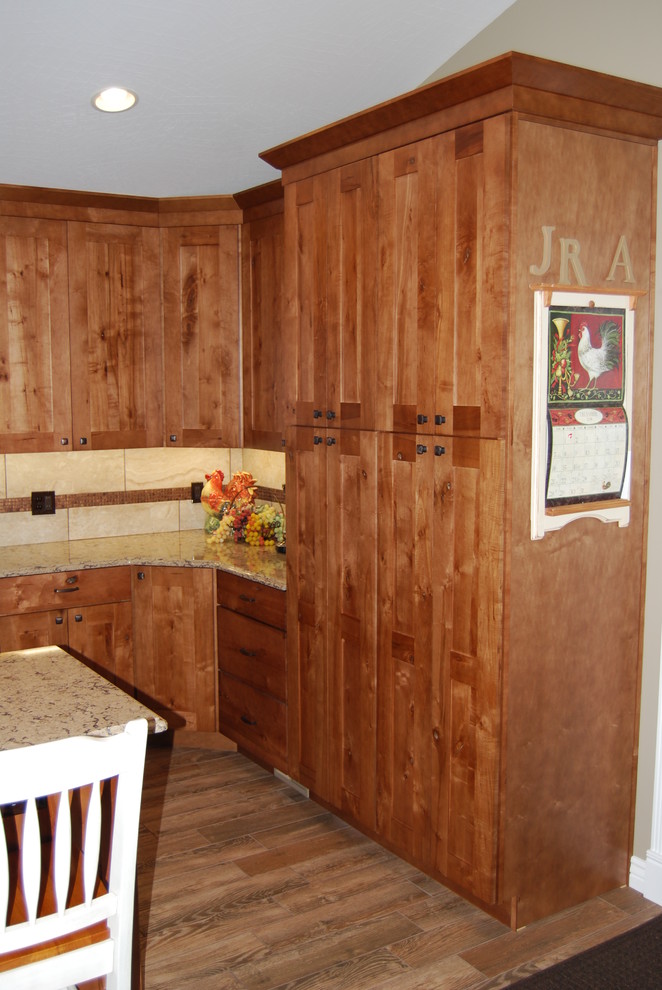 Mid-sized mountain style l-shaped porcelain tile and brown floor eat-in kitchen photo with an undermount sink, medium tone wood cabinets, beige backsplash, porcelain backsplash, shaker cabinets, quartz countertops, stainless steel appliances and an island