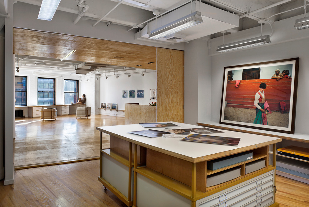 Industrial home studio in New York with white walls, medium hardwood floors and a freestanding desk.