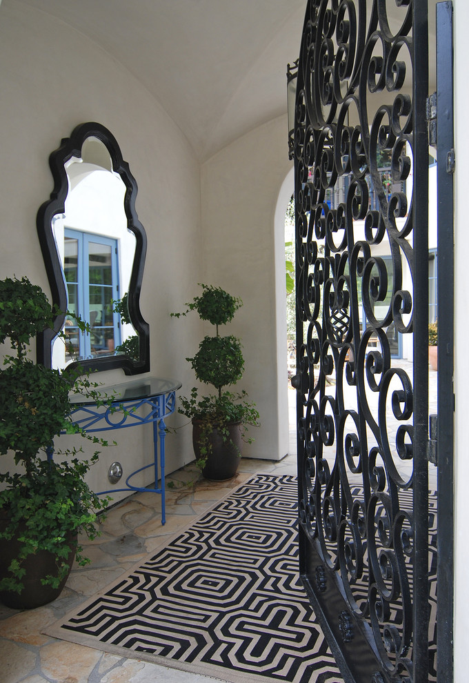 This is an example of a mid-sized mediterranean vestibule in Los Angeles with white walls, slate floors and a black front door.