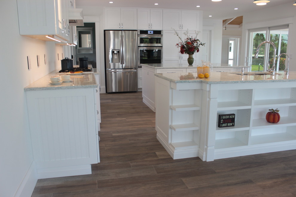 Large beach style single-wall open plan kitchen in Miami with white cabinets, quartz benchtops, white splashback, stainless steel appliances, ceramic floors, multiple islands, a double-bowl sink and shaker cabinets.