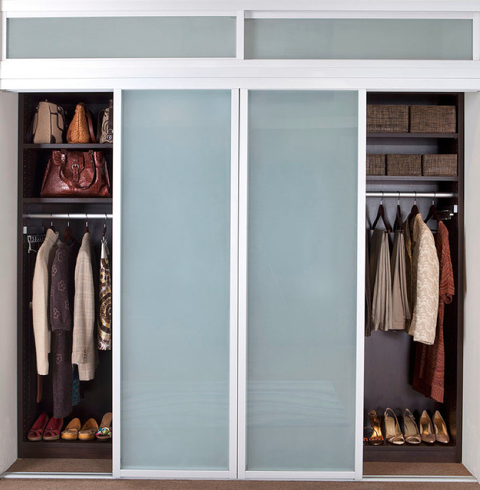 Large modern gender-neutral built-in wardrobe in New York with glass-front cabinets, carpet and dark wood cabinets.
