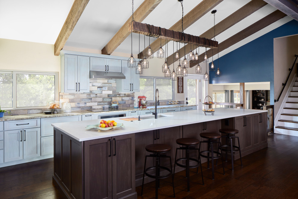 Large industrial galley open plan kitchen in Denver with a submerged sink, flat-panel cabinets, blue cabinets, blue splashback, metro tiled splashback, stainless steel appliances, an island, a vaulted ceiling, engineered stone countertops, medium hardwood flooring and white worktops.