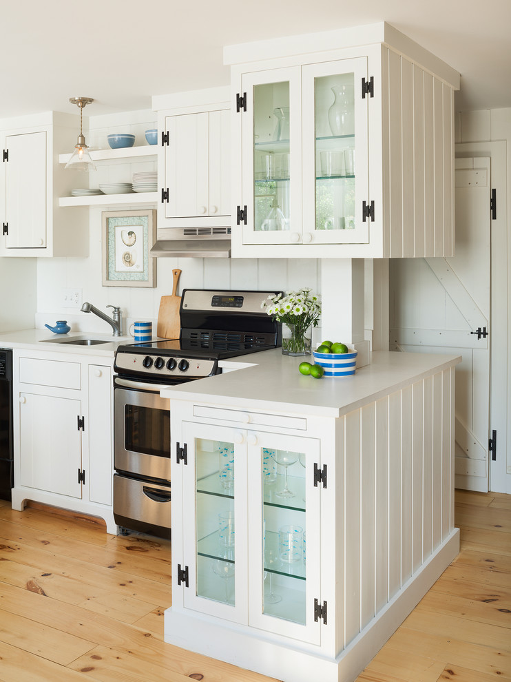 Eat-in kitchen - small coastal l-shaped light wood floor eat-in kitchen idea in Providence with a drop-in sink, glass-front cabinets, white cabinets, solid surface countertops, white backsplash, stainless steel appliances and a peninsula