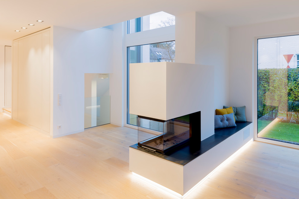 Mid-sized contemporary open concept living room in Dusseldorf with white walls, light hardwood floors, a corner fireplace, a plaster fireplace surround, a built-in media wall and beige floor.