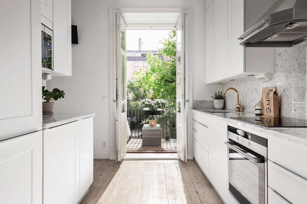 Mid-sized scandinavian galley kitchen in Stockholm with an undermount sink, flat-panel cabinets, white cabinets, grey splashback, stainless steel appliances, light hardwood floors, no island and marble benchtops.