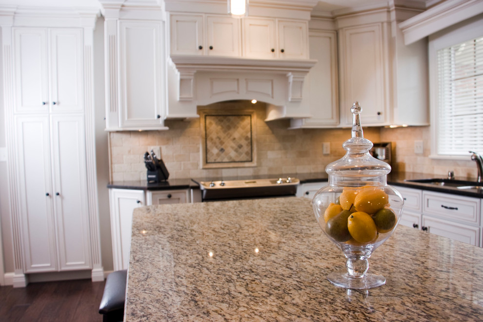 Large transitional u-shaped medium tone wood floor kitchen photo in Cincinnati with an undermount sink, recessed-panel cabinets, white cabinets, granite countertops, beige backsplash, stone tile backsplash, stainless steel appliances and an island