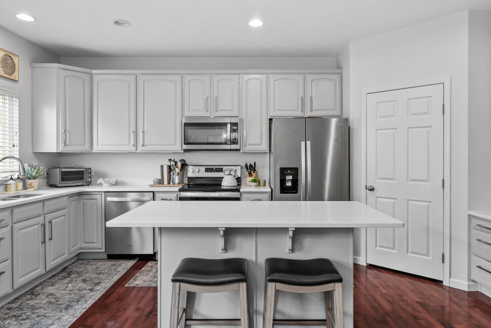 Example of a transitional dark wood floor eat-in kitchen design with a double-bowl sink, gray cabinets, quartz countertops, stainless steel appliances, an island and white countertops