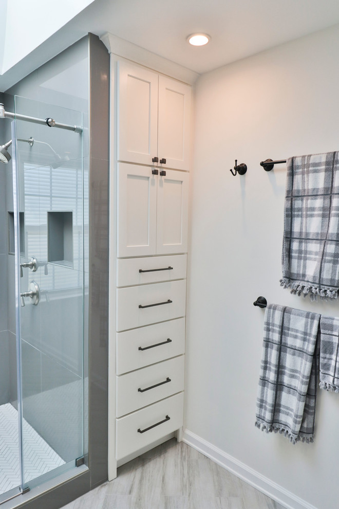 This is an example of a mid-sized transitional 3/4 bathroom in DC Metro with shaker cabinets, white cabinets, an alcove shower, grey walls, vinyl floors, an undermount sink, marble benchtops, grey floor, a hinged shower door and white benchtops.