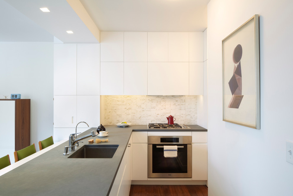 Inspiration for a small modern l-shaped eat-in kitchen in New York with an undermount sink, flat-panel cabinets, white cabinets, limestone benchtops, stone tile splashback, panelled appliances, medium hardwood floors, a peninsula and white splashback.